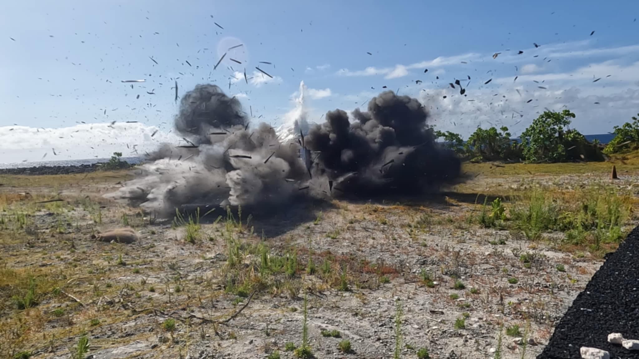 Powerful explosion erupting in a dry field, scattering thick black smoke and debris everywhere.